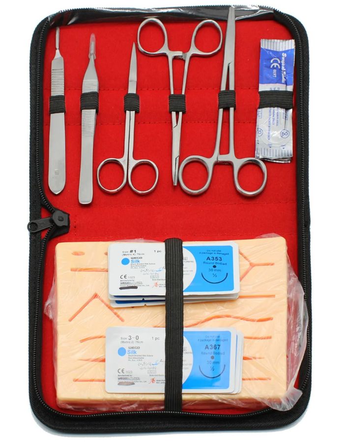 A surgical instrument set organized inside a black zippered case with a bright red interior. The set includes several silver metal surgical tools such as scissors and forceps, along with packaged sterile items and gauze packs secured by a black elastic band.